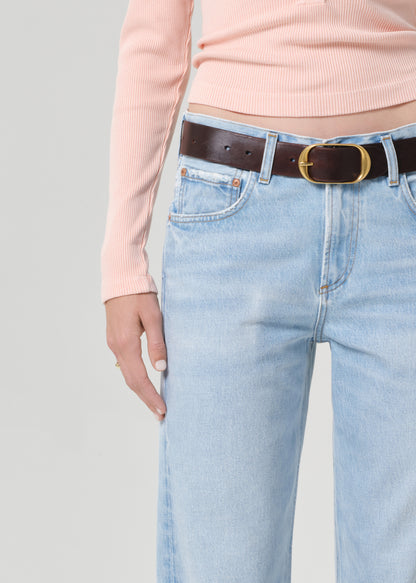 Person wearing a light pink long-sleeve shirt and light blue jeans on a grey background