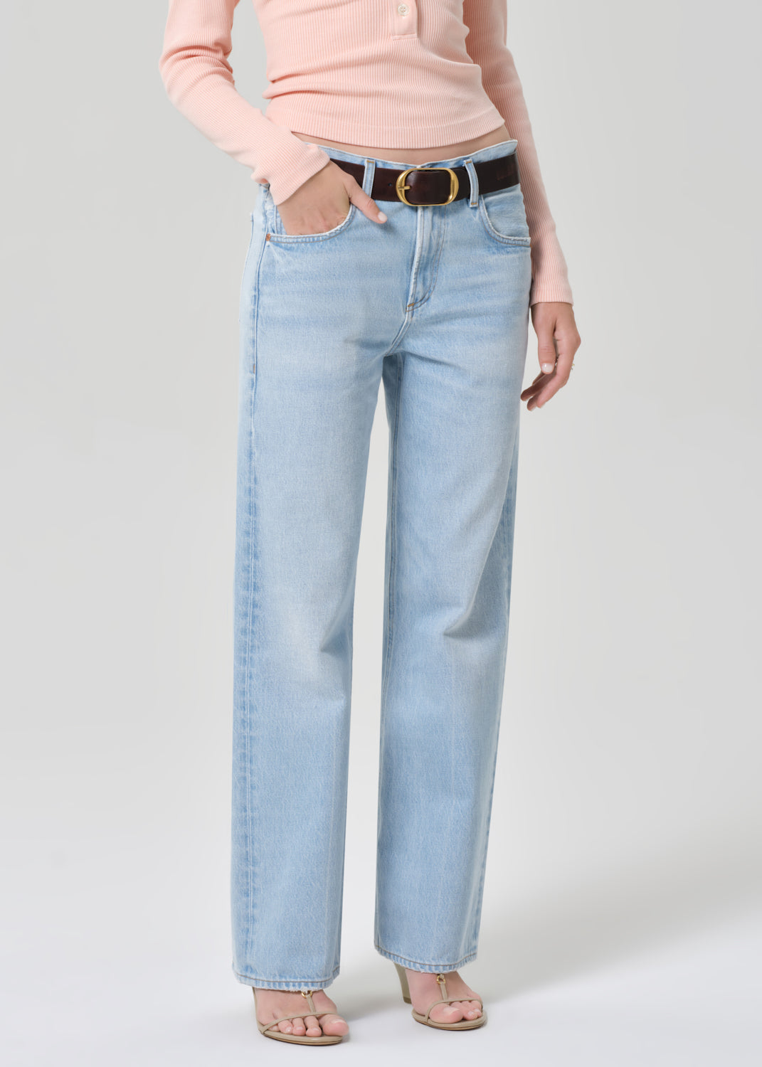 Person wearing a light pink long-sleeve shirt and light blue jeans on a grey background