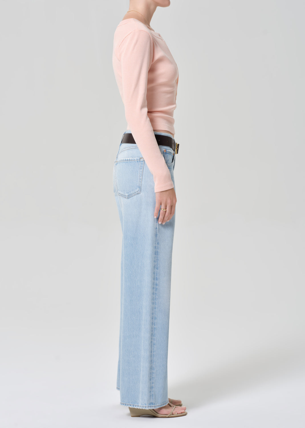 Person wearing a light pink long-sleeve shirt and light blue jeans on a grey background