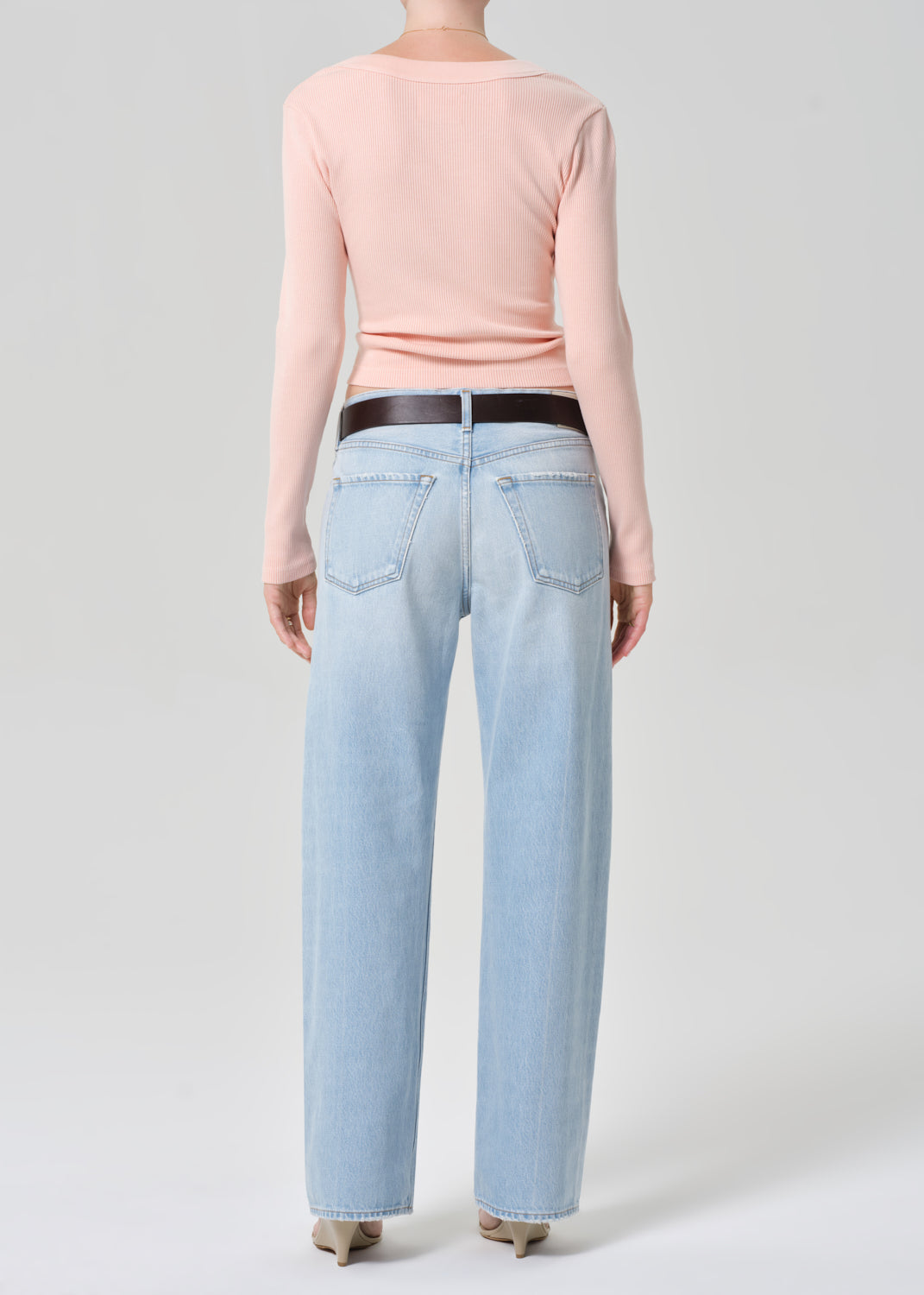 Person wearing a light pink long-sleeve shirt and light blue jeans on a grey background