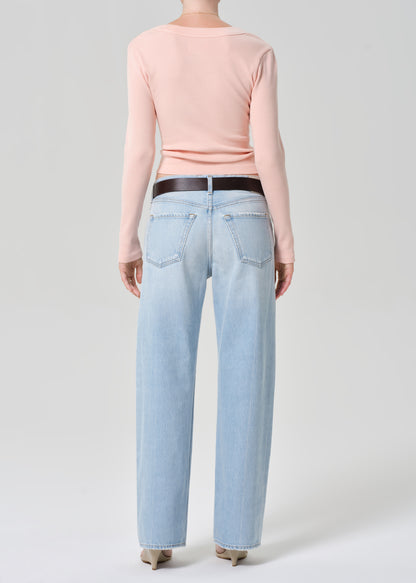 Person wearing a light pink long-sleeve shirt and light blue jeans on a grey background