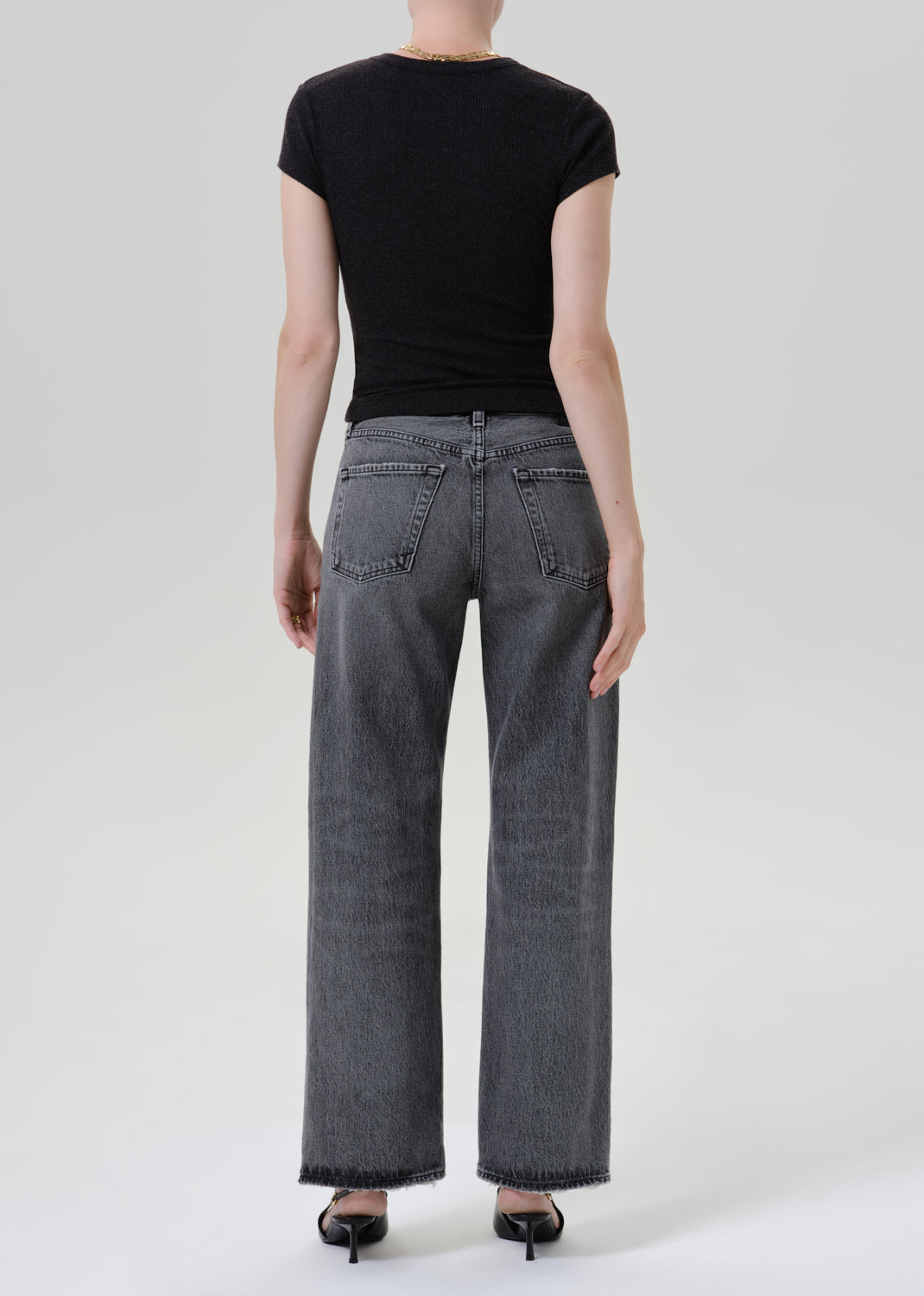 Person wearing black t-shirt with grey denim pants on a grey background