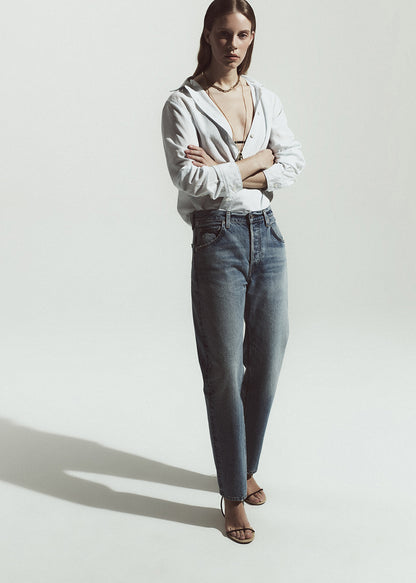 Woman wearing a white shirt with stripes and blue jeans standing against a plain background