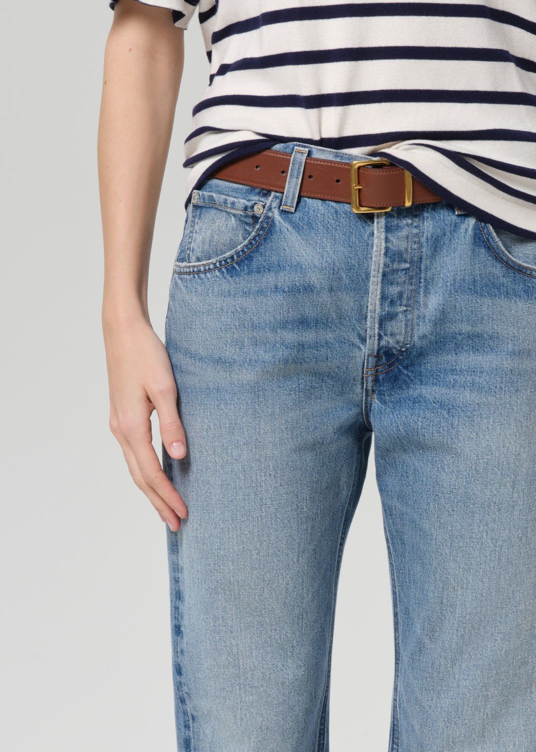 Person wearing a striped shirt and blue jeans with a brown belt on a plain background