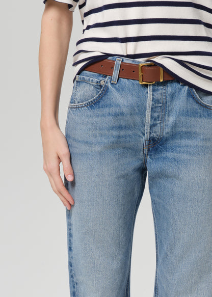 Person wearing a striped shirt and blue jeans with a brown belt on a plain background