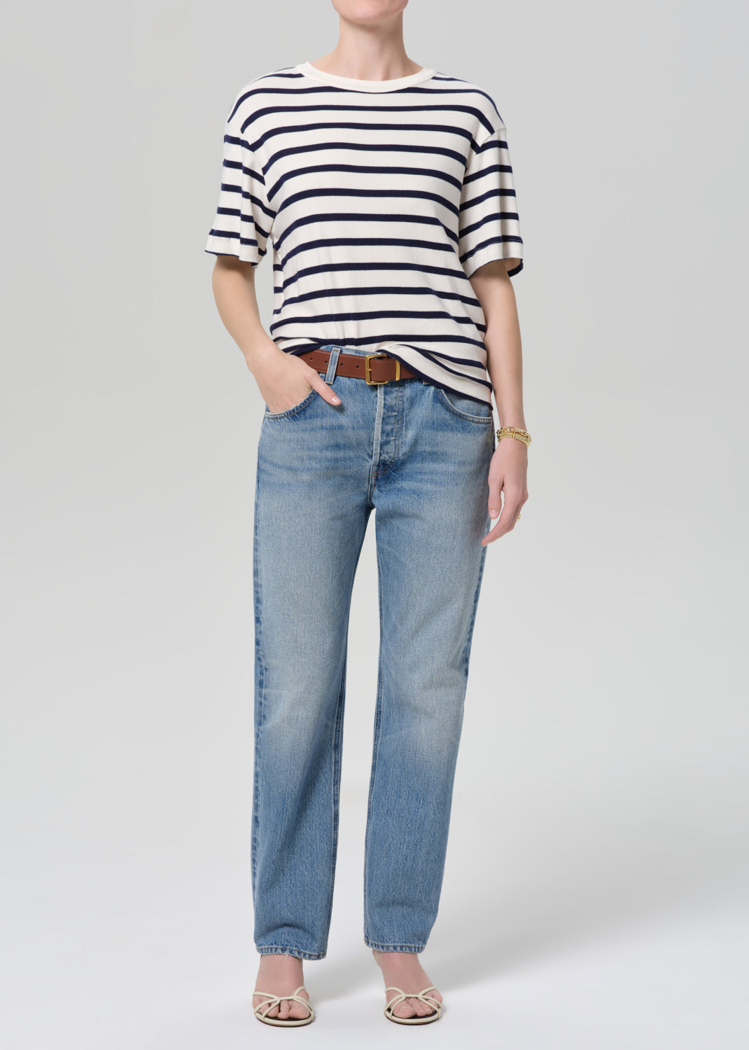 Person wearing a striped shirt and blue jeans on a plain background