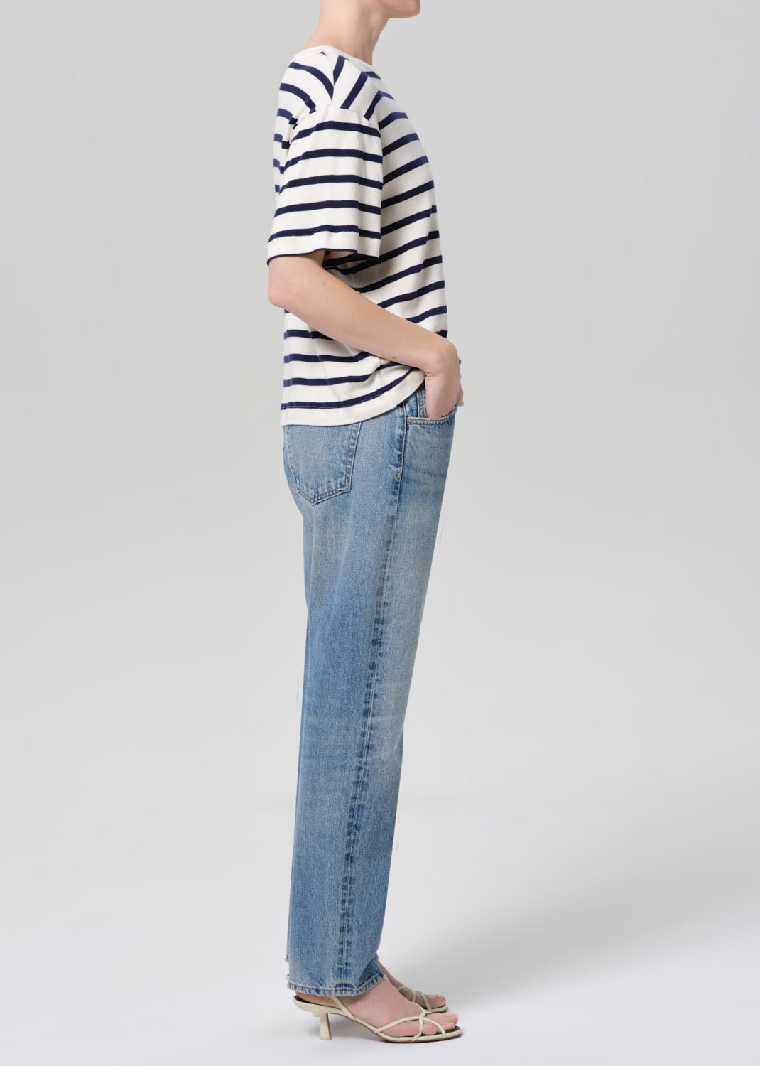 Person wearing a striped shirt and blue jeans on a plain background