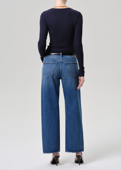 A model shown from the back wearing a navy long-sleeve top, blue wide-leg jeans, a black belt, and black heels against a grey background.