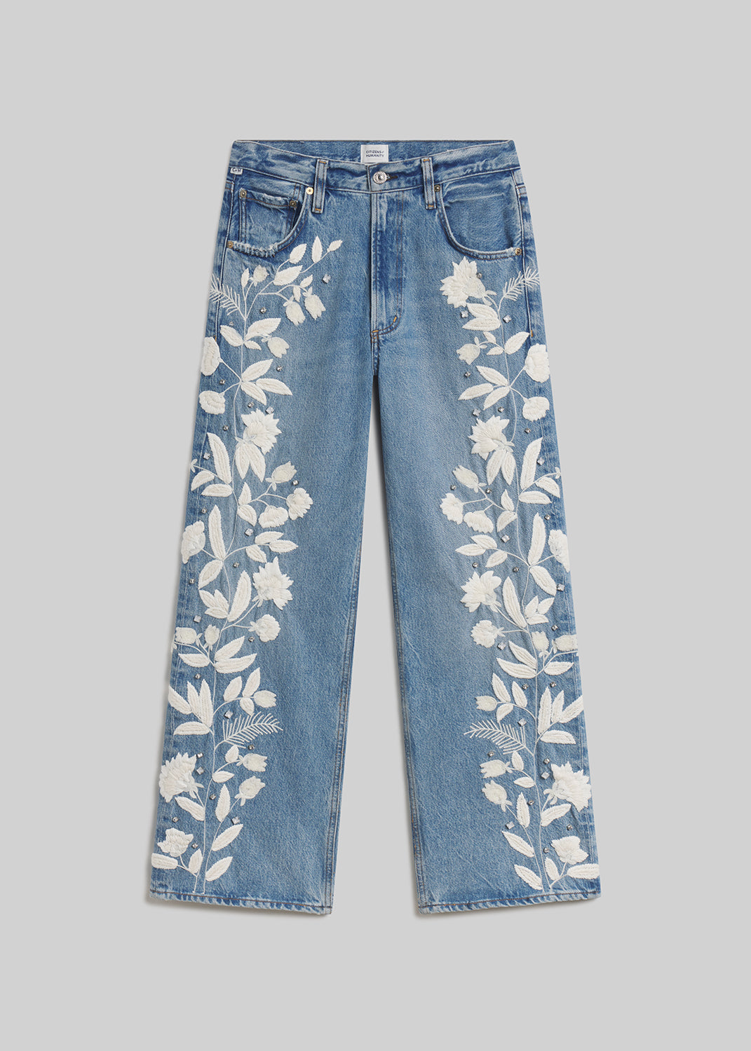 Blue wide-leg jeans with white floral embroidery on grey background