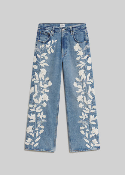 Blue wide-leg jeans with white floral embroidery on grey background