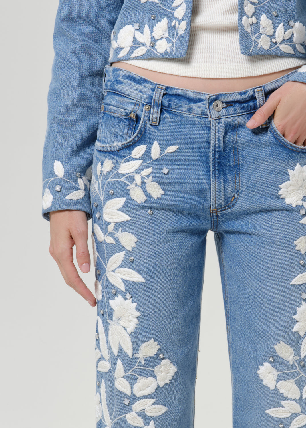 Close-up of light blue floral jeans on a grey background.