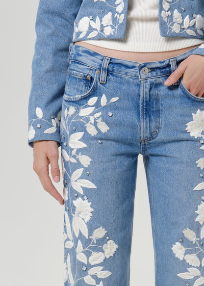 Close-up of light blue floral jeans on a grey background.