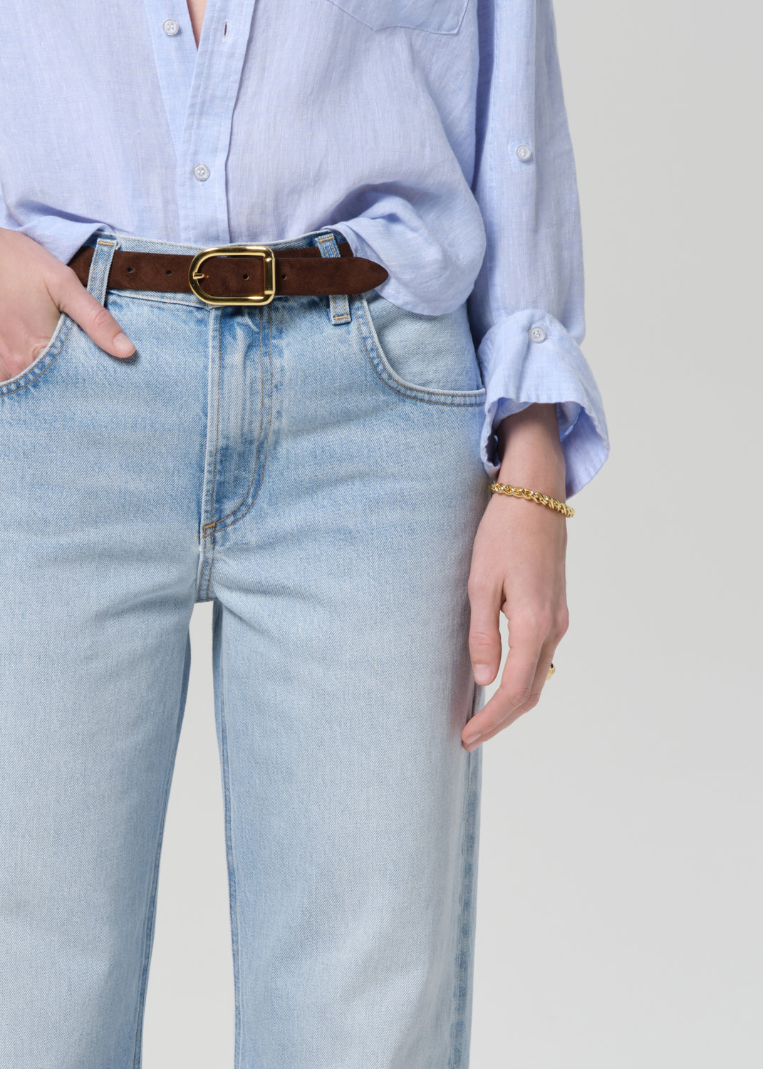 Person wearing a light blue shirt and jeans on a grey background