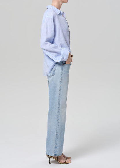 Person wearing a light blue shirt and jeans on a grey background
