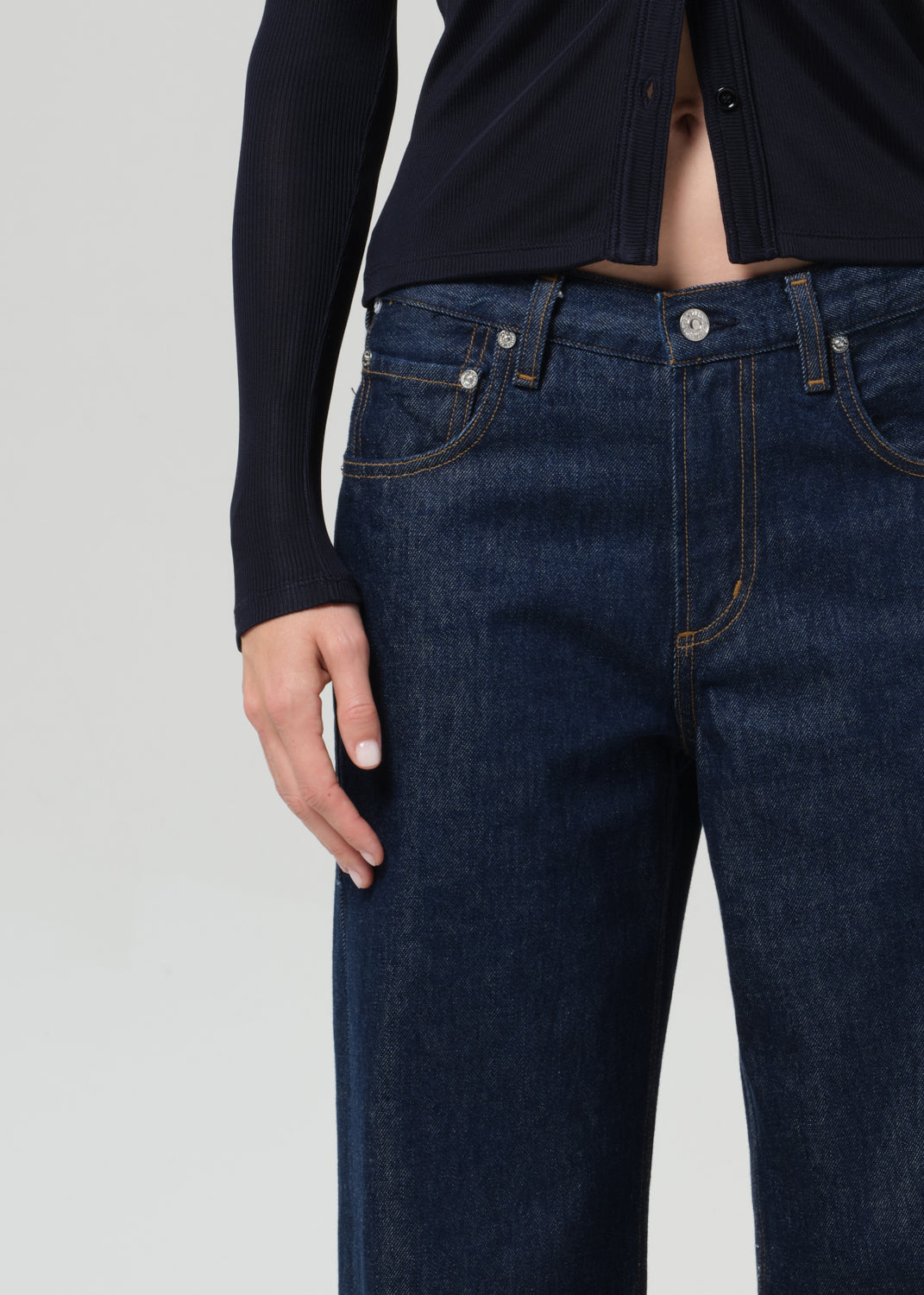 Person wearing a navy shirt and dark blue jeans on a grey background