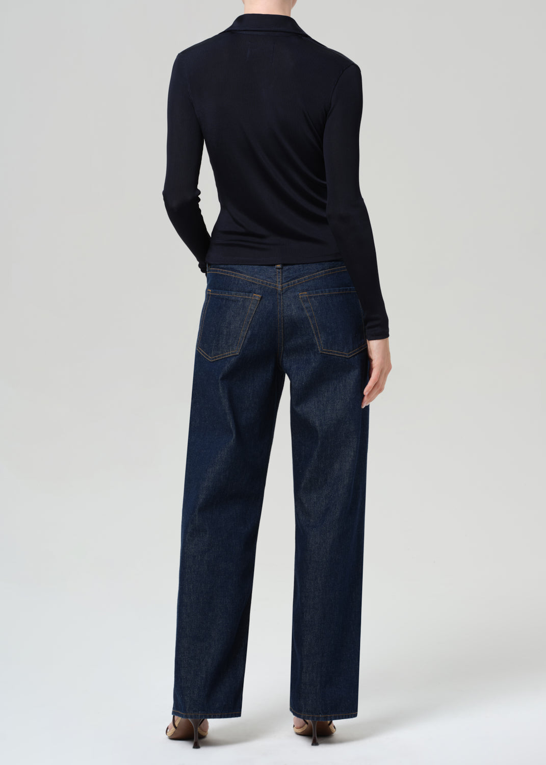 Person wearing a navy shirt and dark blue jeans on a grey background