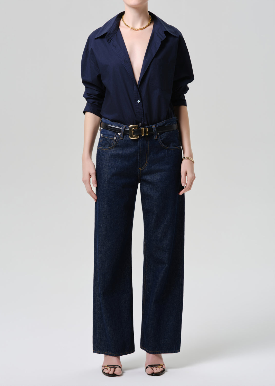 Person wearing a navy shirt and dark jeans with a belt on a grey background