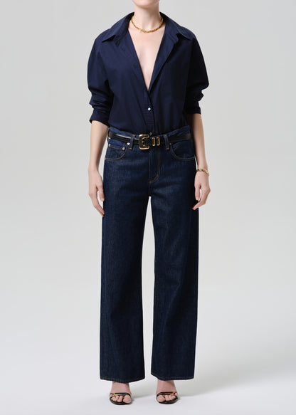 Person wearing a navy shirt and dark jeans with a belt on a grey background