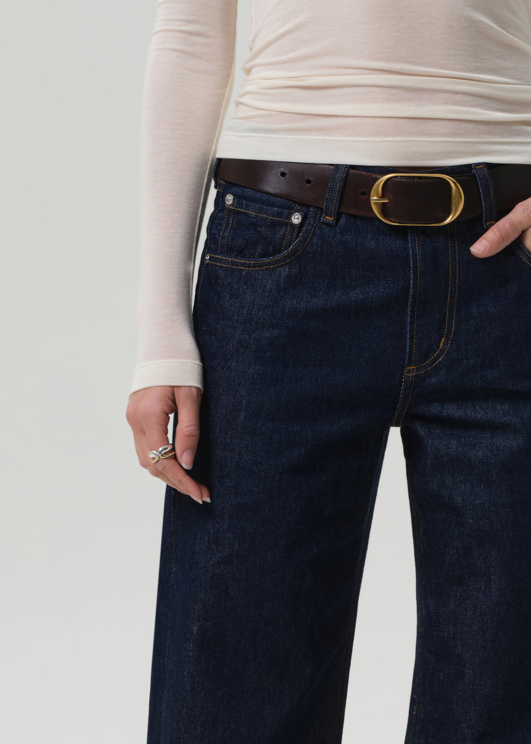 Person wearing dark blue jeans with a brown belt on a light gray background