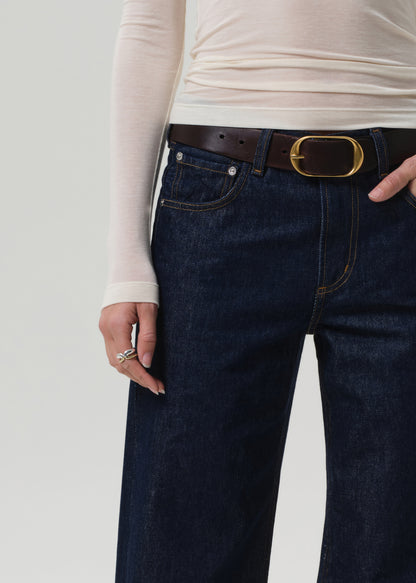 Person wearing dark blue jeans with a brown belt on a light gray background