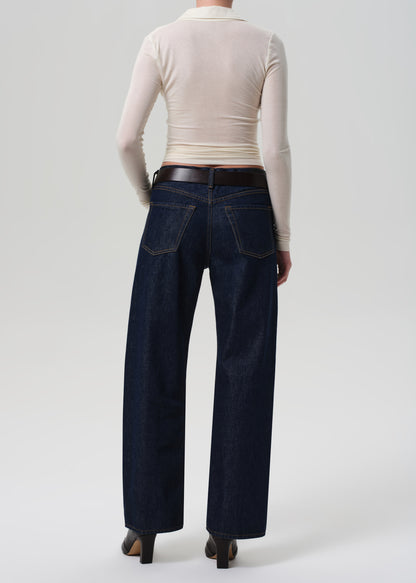 Person wearing a beige long-sleeve top and dark blue jeans on a white background