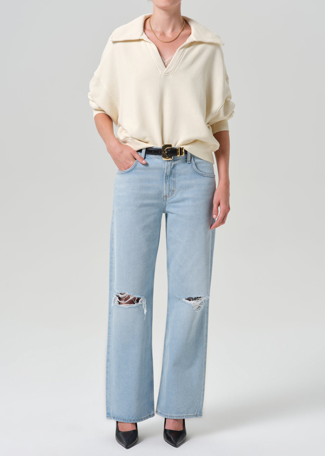 Person wearing beige sweater with blue pants on a grey background