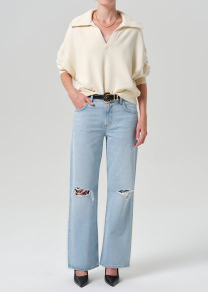 Person wearing beige sweater with blue pants on a grey background