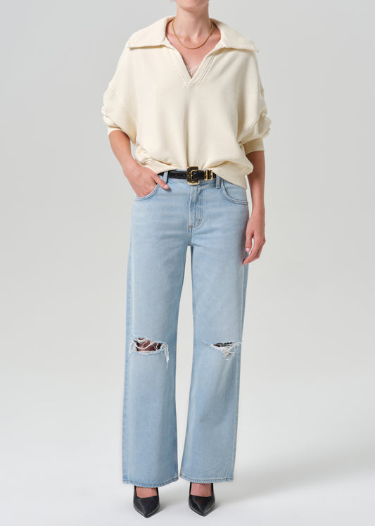Person wearing beige sweater with blue pants on a grey background