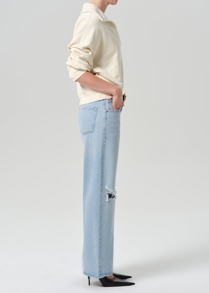 Person wearing beige sweater with blue pants on a grey background