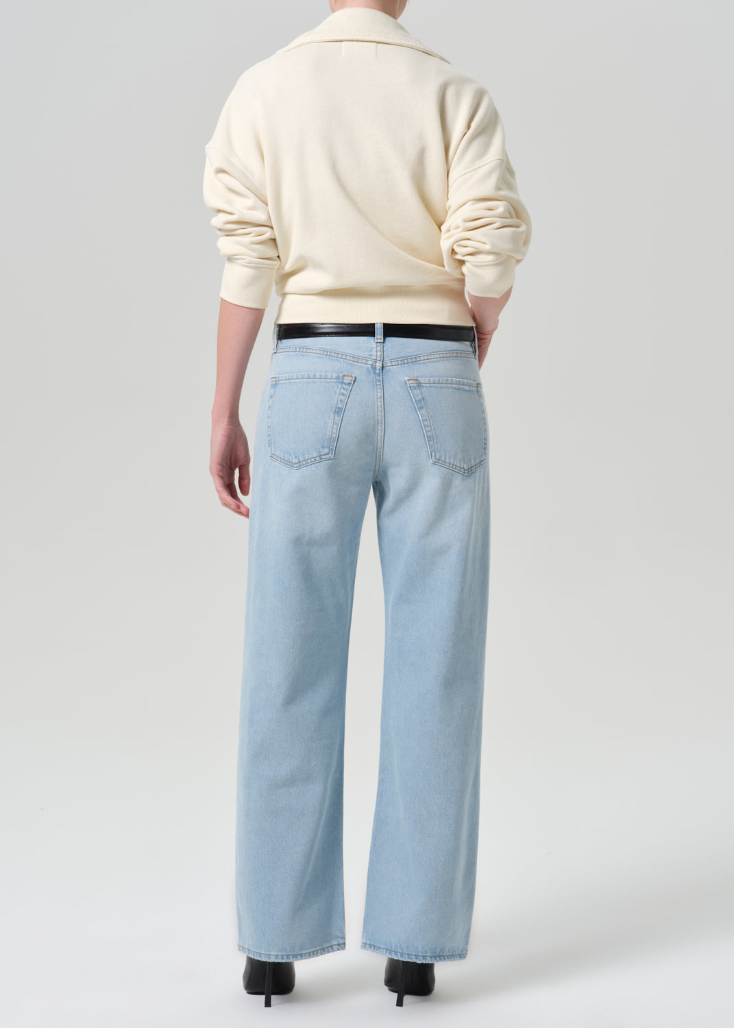 Person wearing beige sweater with blue pants on a grey background