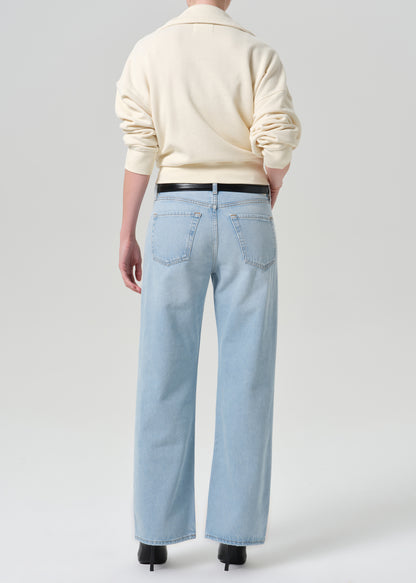Person wearing beige sweater with blue pants on a grey background