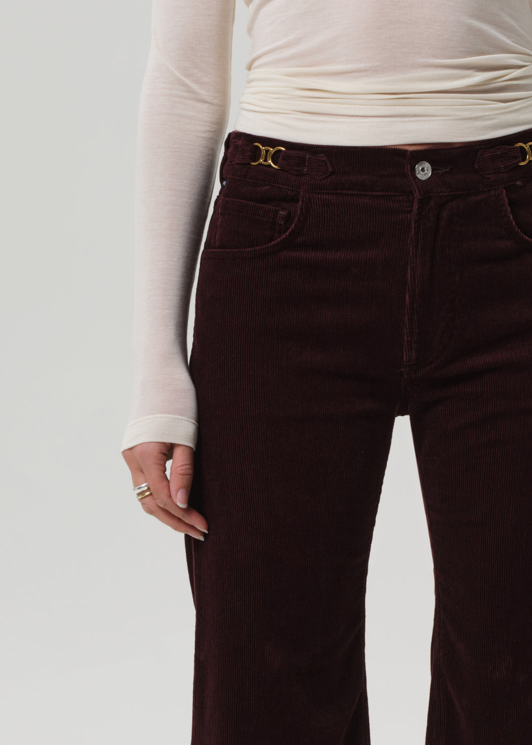 Brown velvet pants worn with a white long-sleeve shirt on a plain background