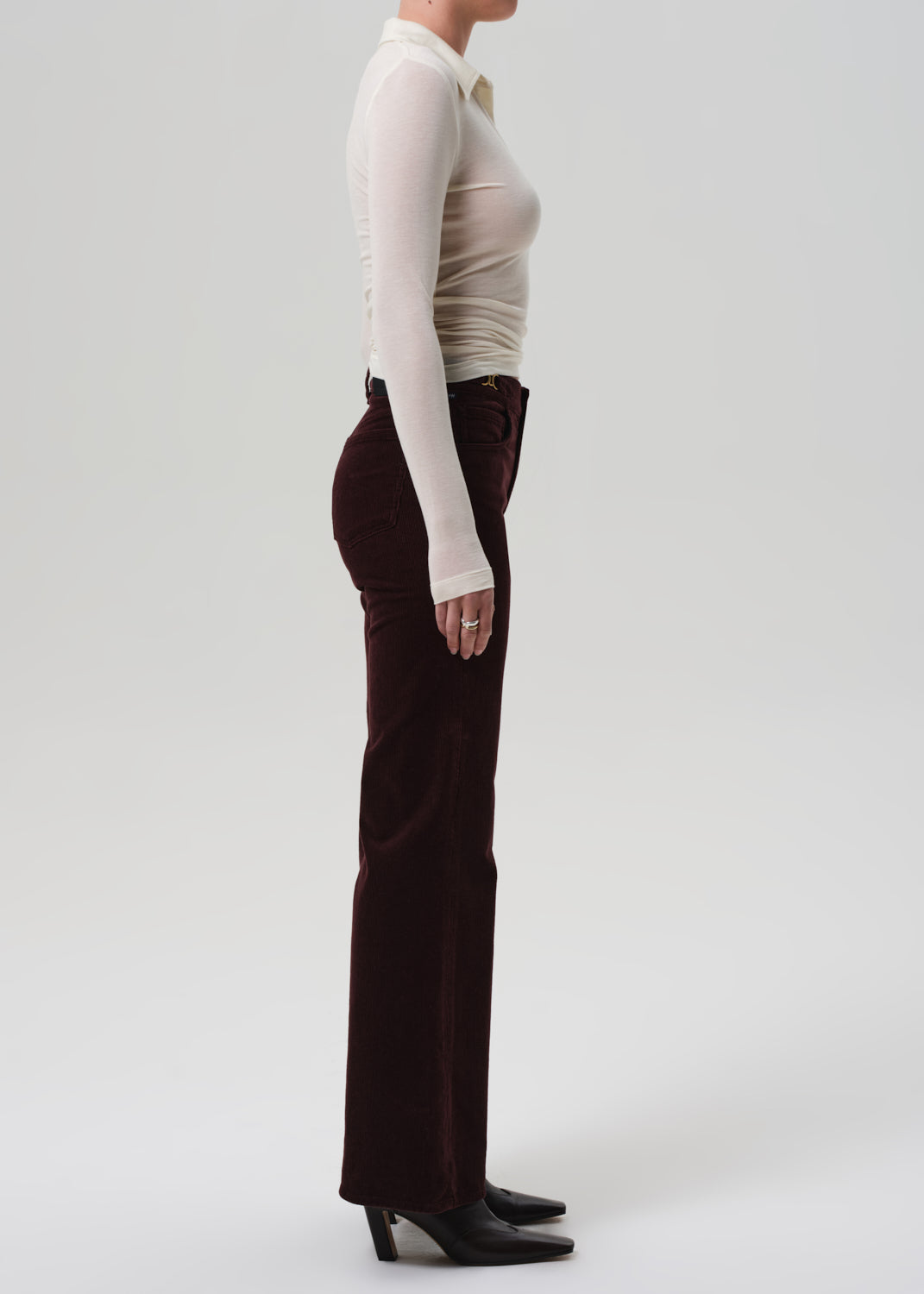 Person wearing a beige long-sleeve top and brown flared pants on a grey background