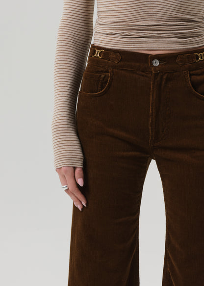 Person wearing a beige ribbed sweater and brown corduroy pants on a grey background