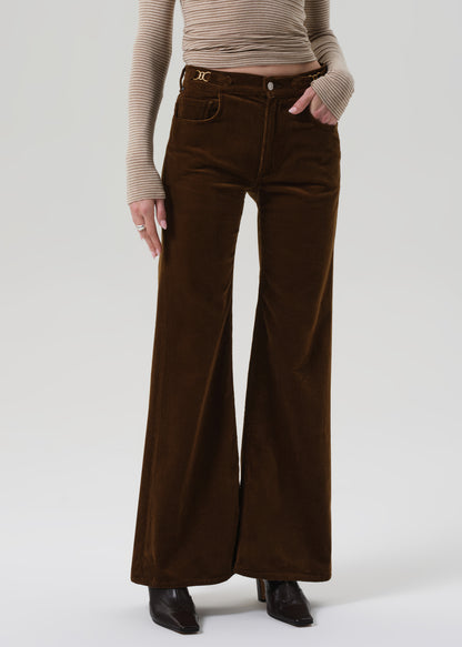 Person wearing a beige ribbed sweater and brown corduroy pants on a grey background