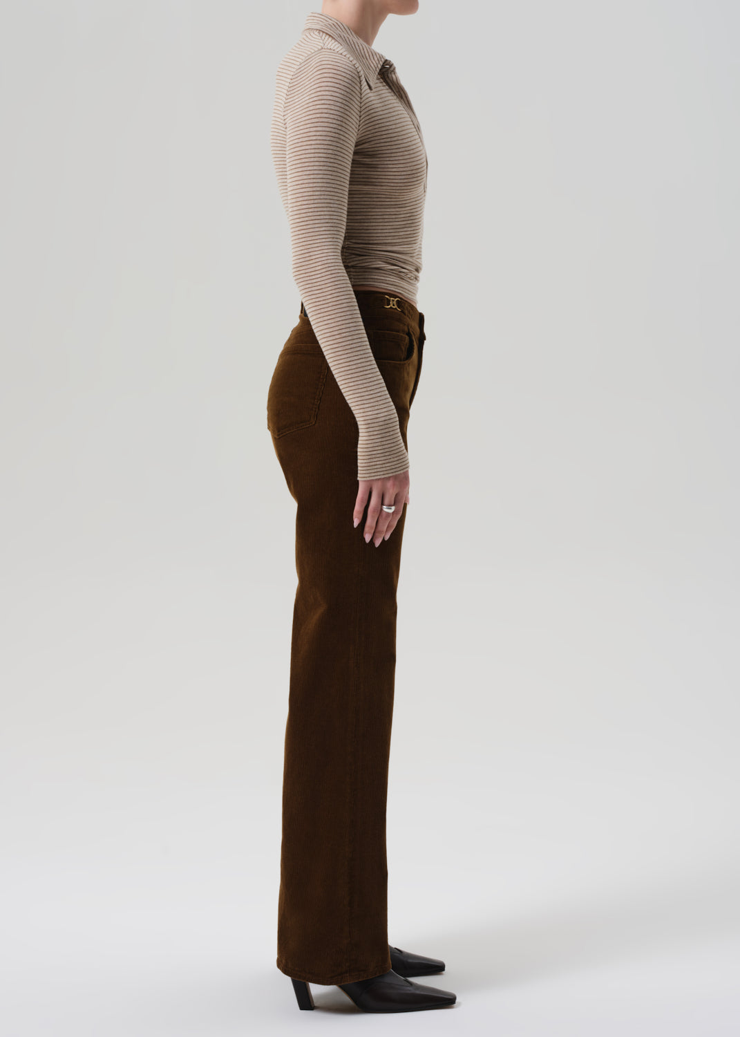 Person wearing a beige ribbed sweater and brown corduroy pants on a grey background