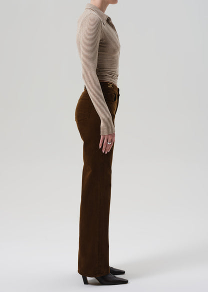 Person wearing a beige ribbed sweater and brown corduroy pants on a grey background