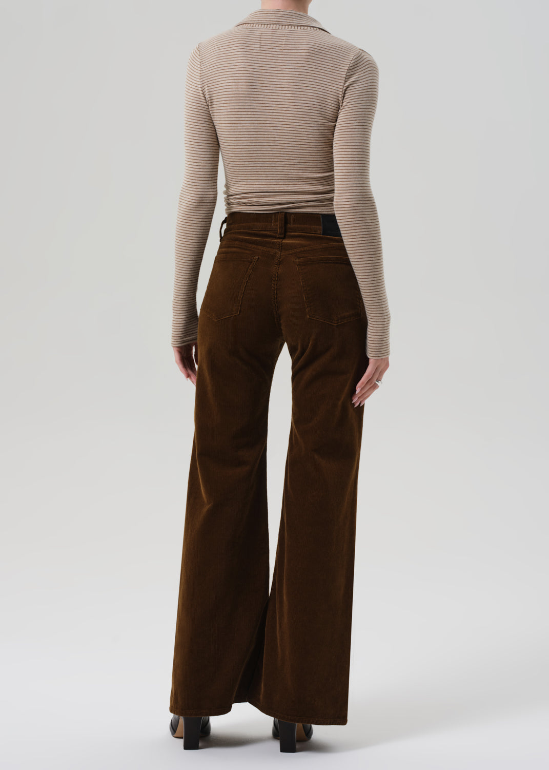 Person wearing a beige ribbed sweater and brown corduroy pants on a grey background