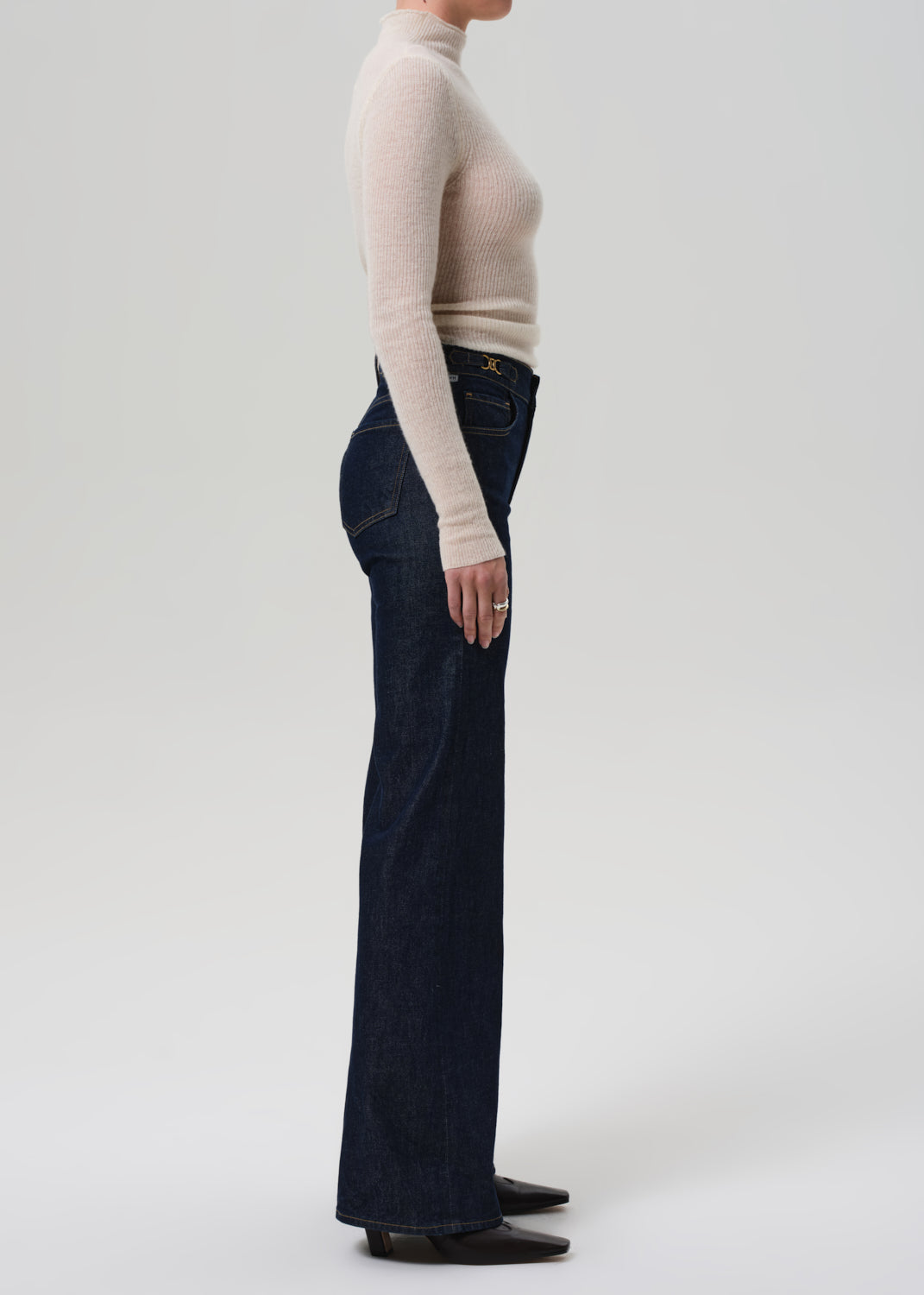 Person wearing a beige sweater and dark blue jeans on a white background