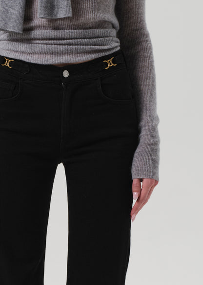 Person wearing black pants with gold buttons and a gray sweater on a light gray background