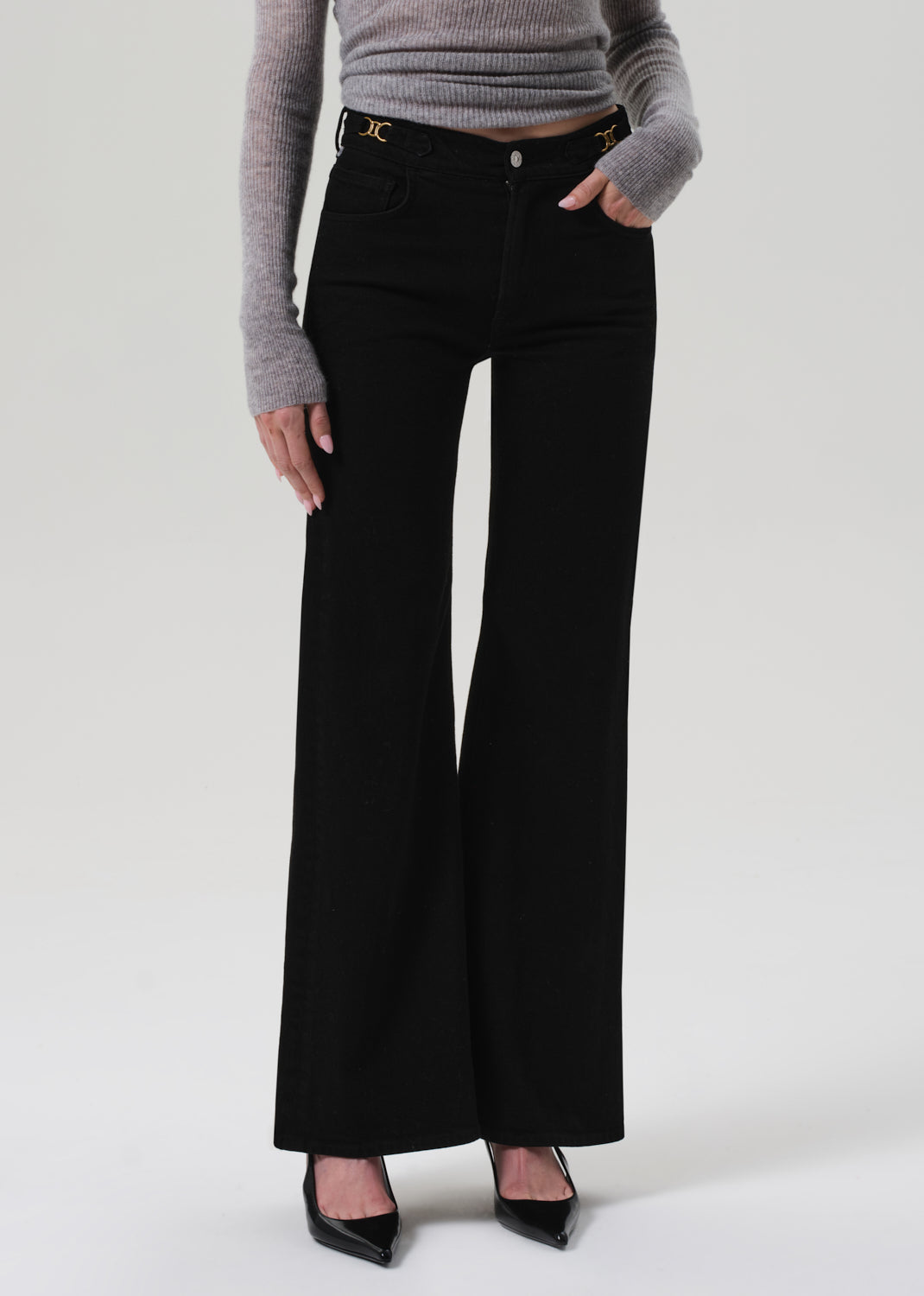 Person wearing black flared jeans and a gray sweater on a white background