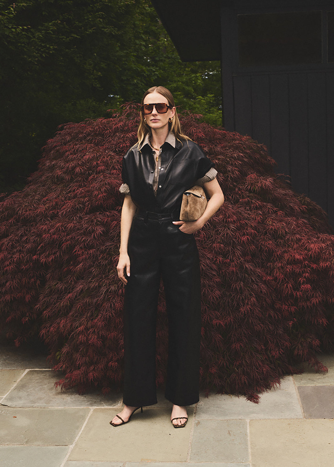 Woman in a black outfit standing outdoors with a red bush in the background