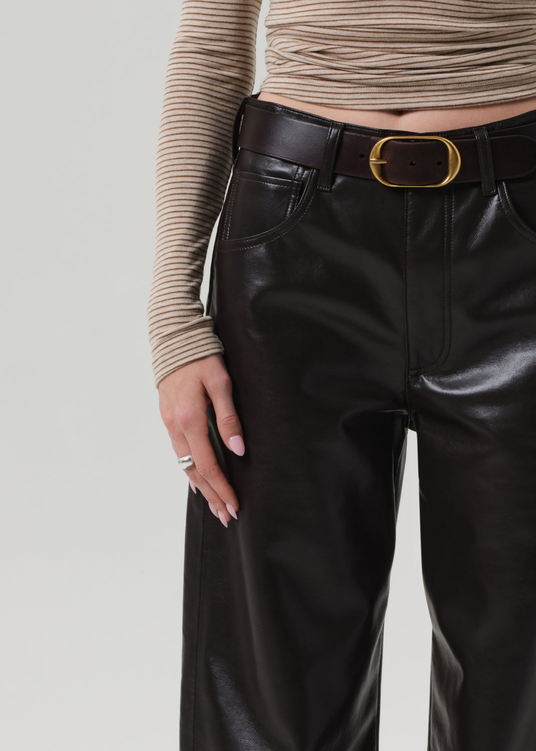 Person wearing a beige turtleneck and brown leather pants on a grey background