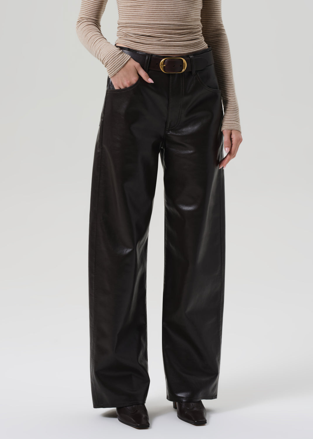 Person wearing a beige turtleneck and brown leather pants on a grey background