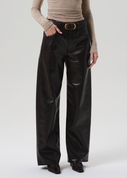 Person wearing a beige turtleneck and brown leather pants on a grey background