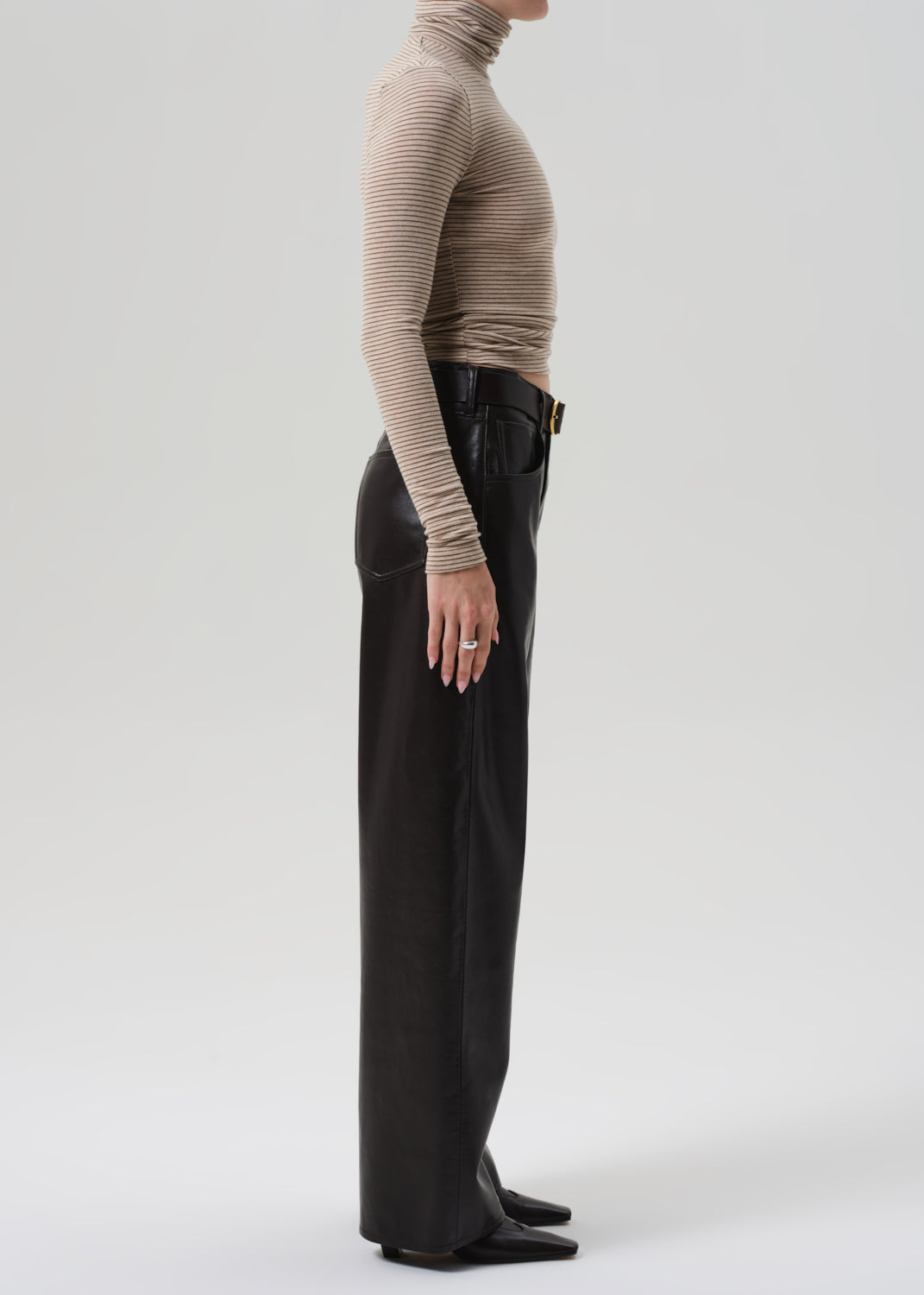 Person wearing a beige turtleneck and brown leather pants on a grey background