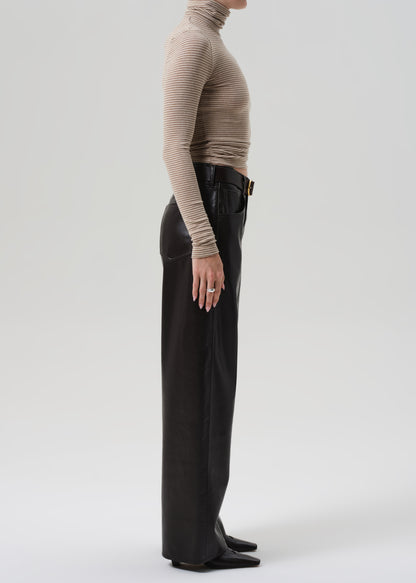 Person wearing a beige turtleneck and brown leather pants on a grey background