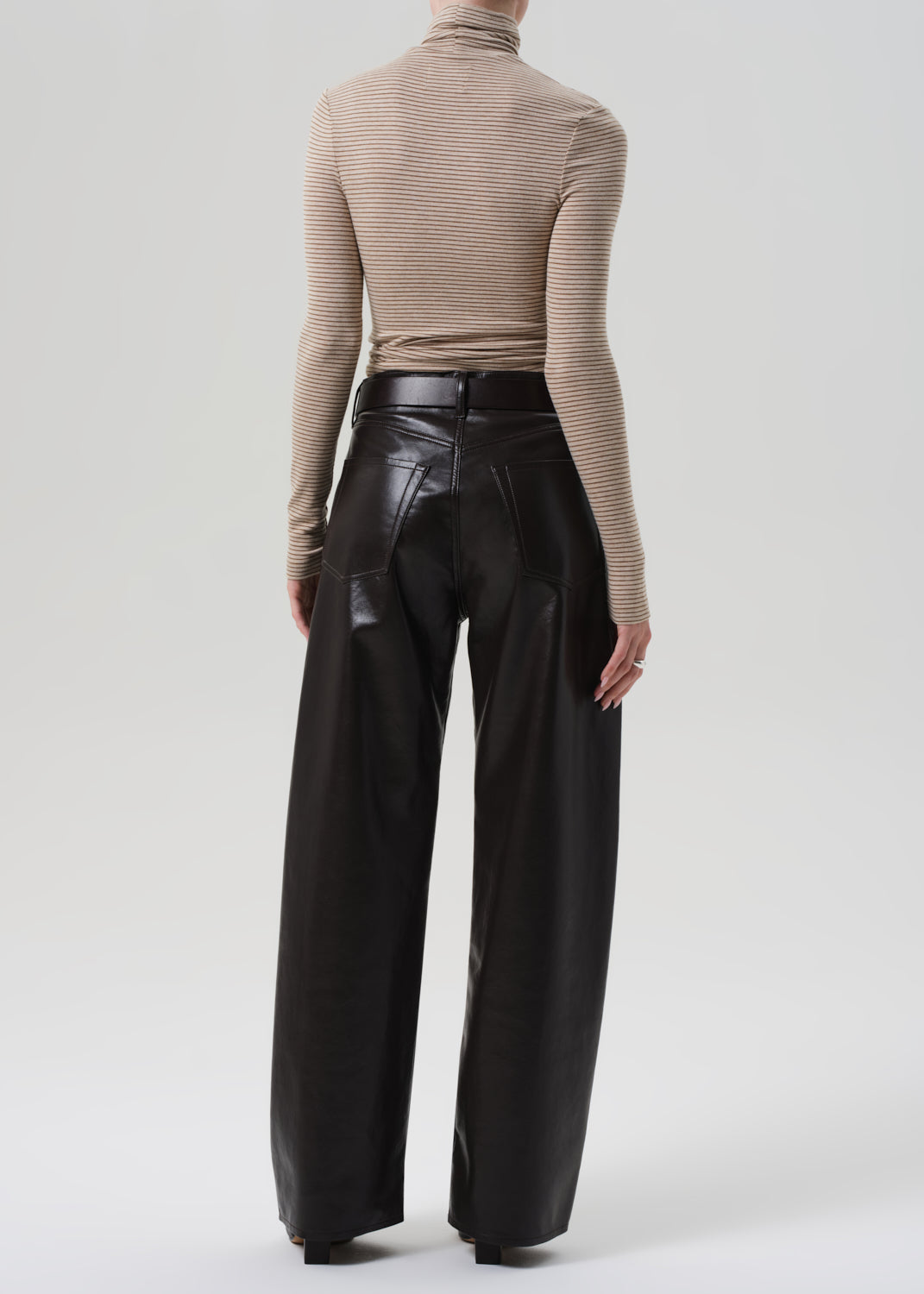 Person wearing a beige turtleneck and brown leather pants on a grey background