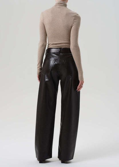 Person wearing a beige turtleneck and brown leather pants on a grey background