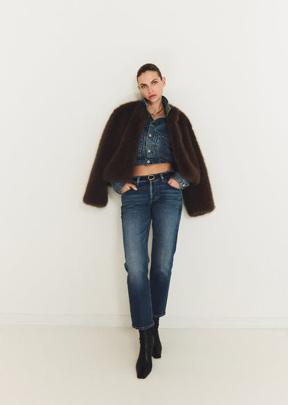 Person wearing a dark brown coat, denim jacket, jeans, and black boots on a white background